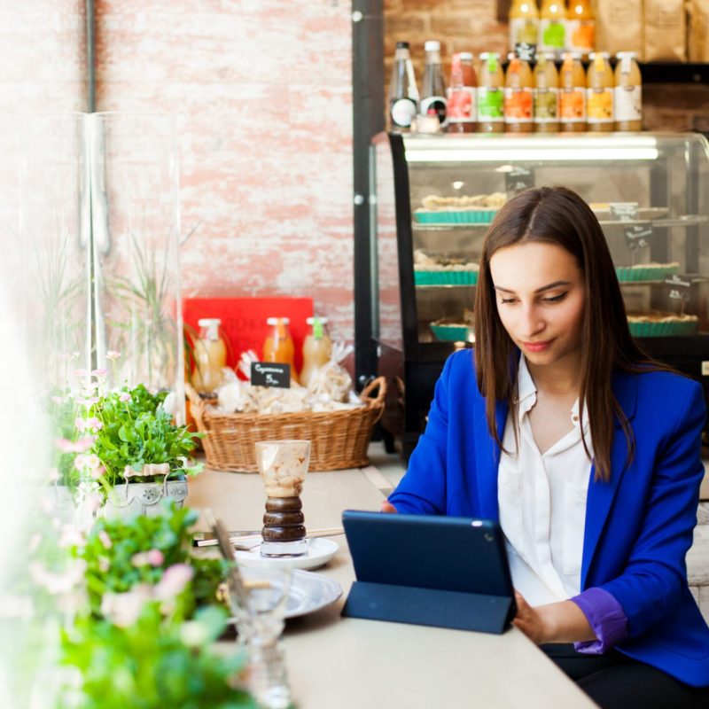 Woman works with a tablet at the table in a cafe